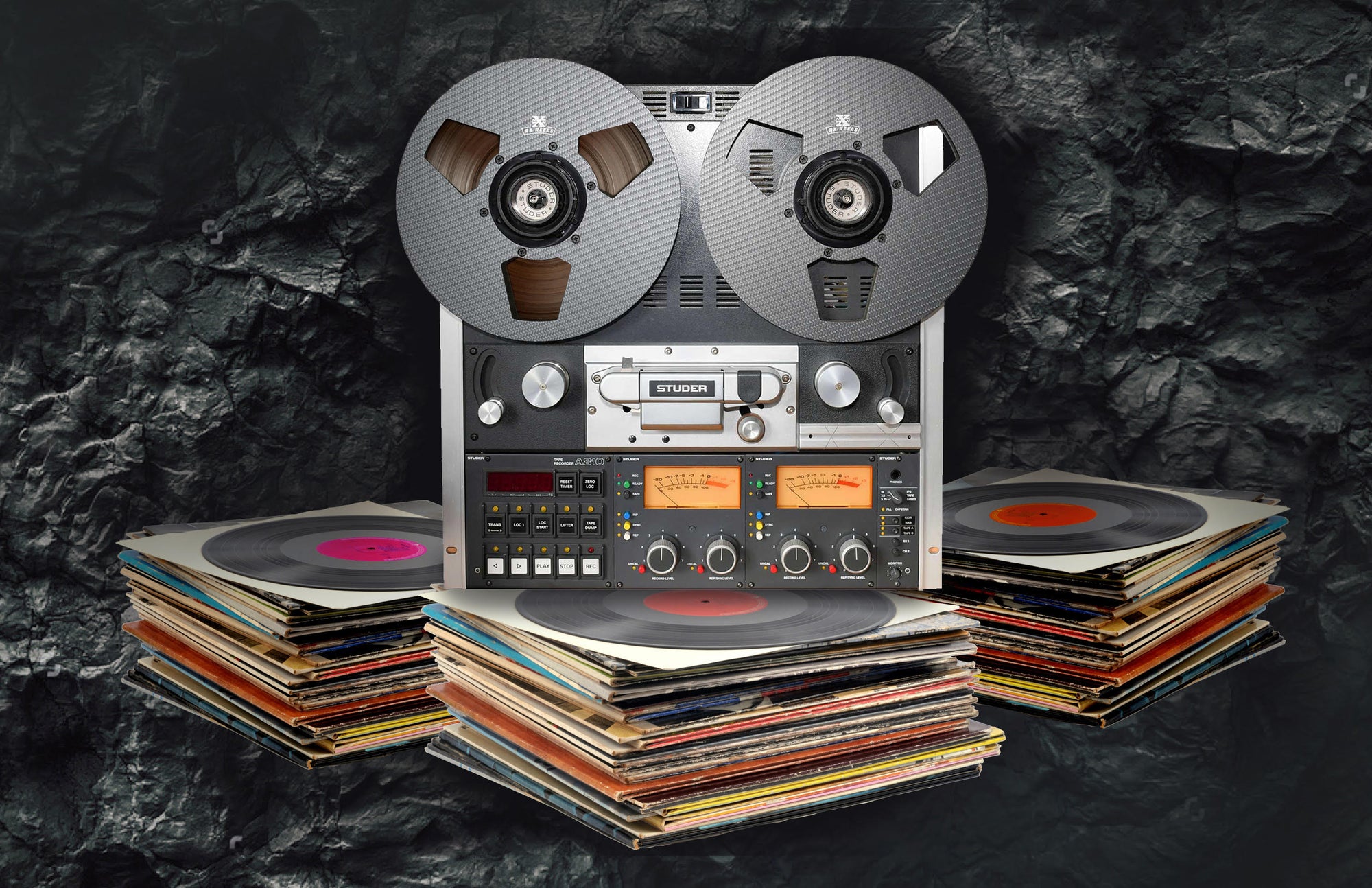 Reel to reel player sits atop a stack of vinyl LPs